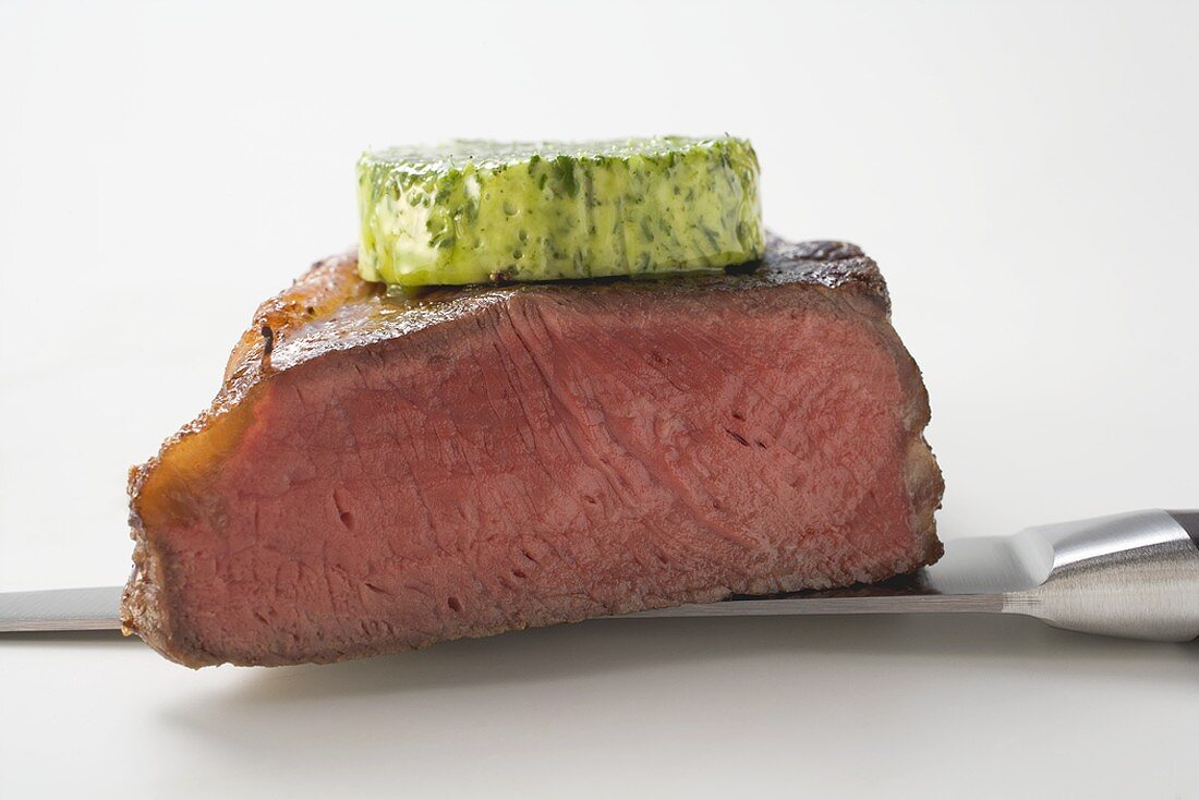 Beef steak with herb butter on knife (showing cut edge)