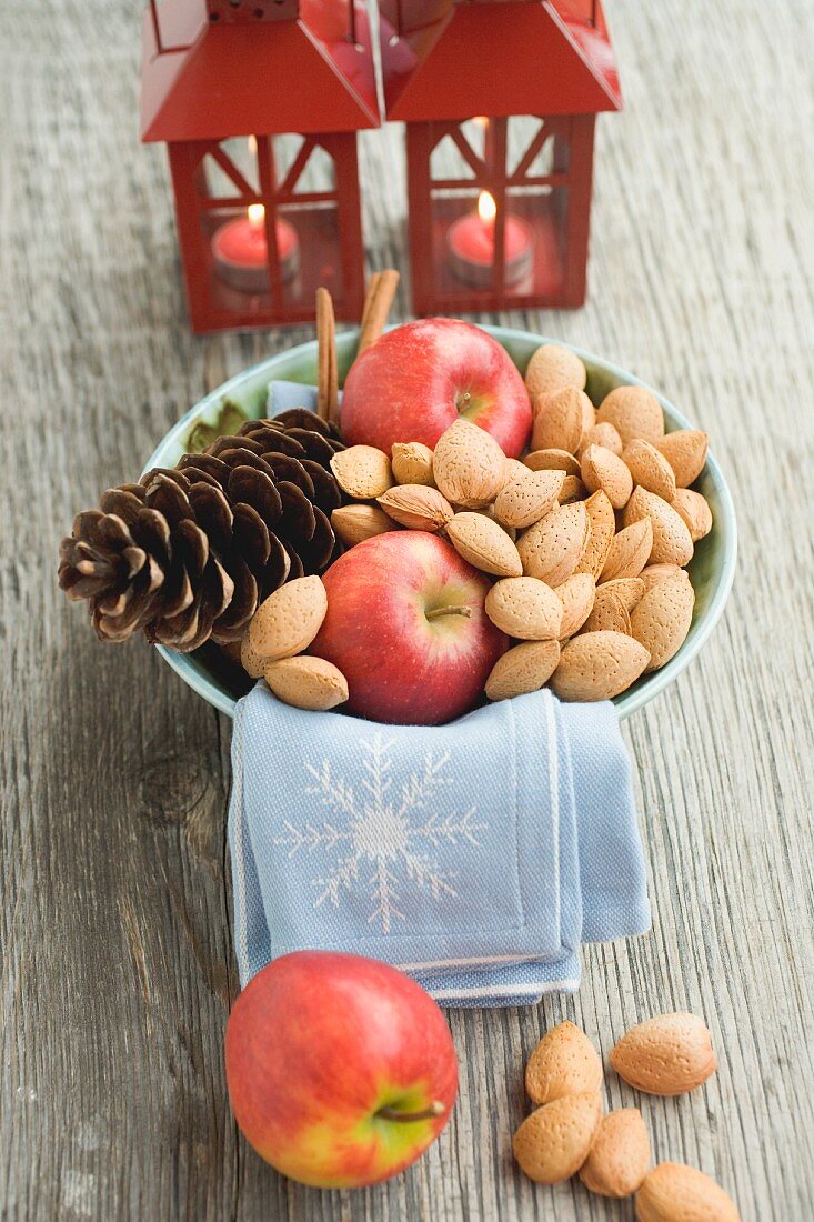 Red apples, almonds and cone in bowl in front of lanterns