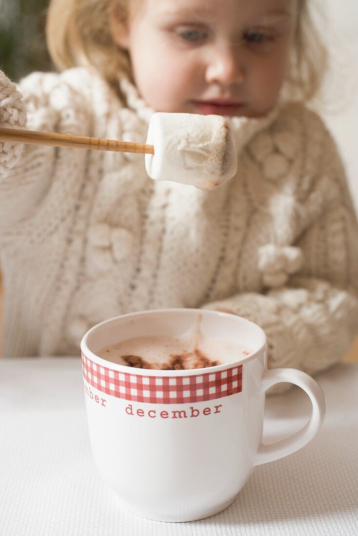 Small girl dipping marshmallow in cocoa