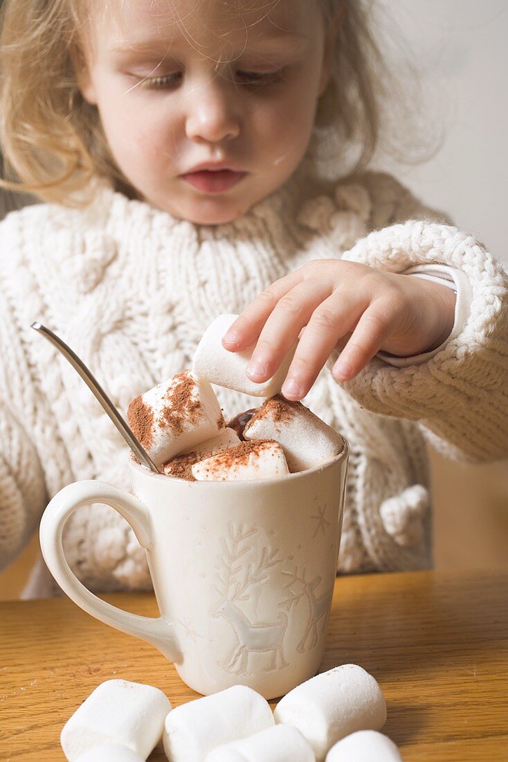 Kleines Mädchen stapelt Marshmallows in Kakaotasse