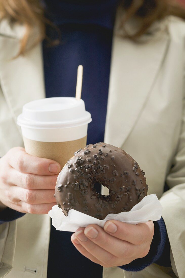 Woman holding chocolate doughnut and cup of coffee