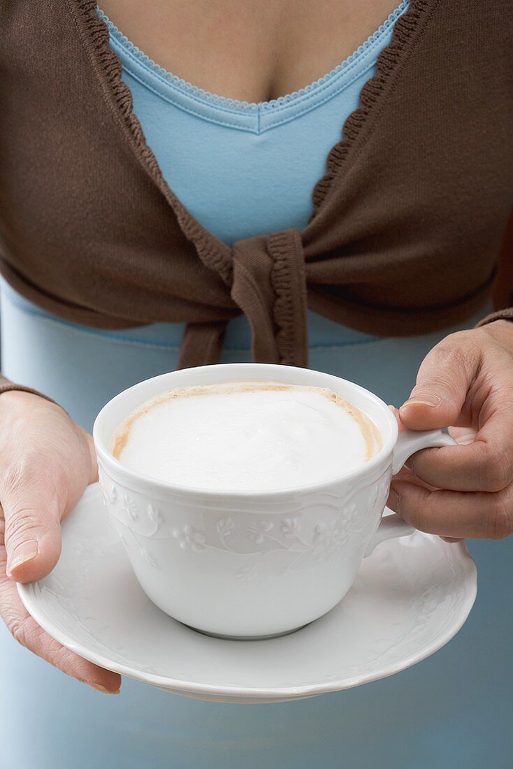 Frau hält Tasse Cappuccino