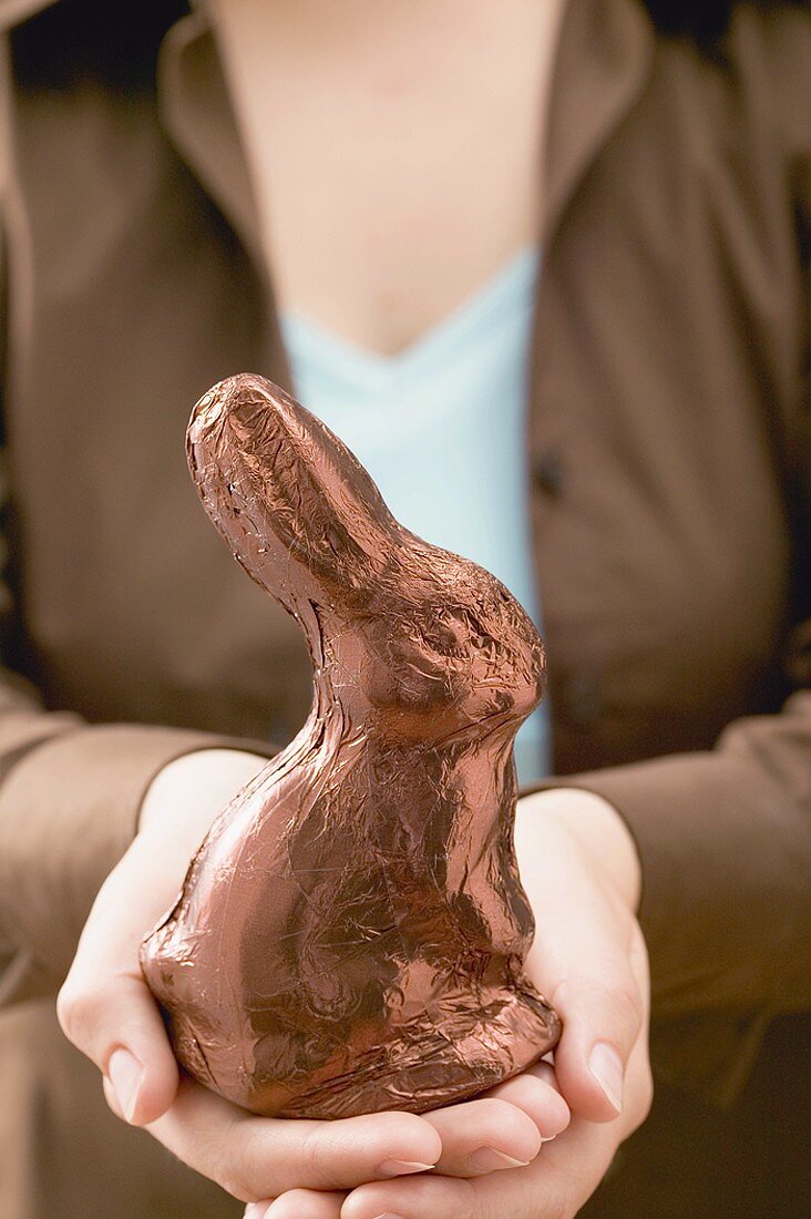 Frau hält in Folie verpackten Schokoladenosterhasen