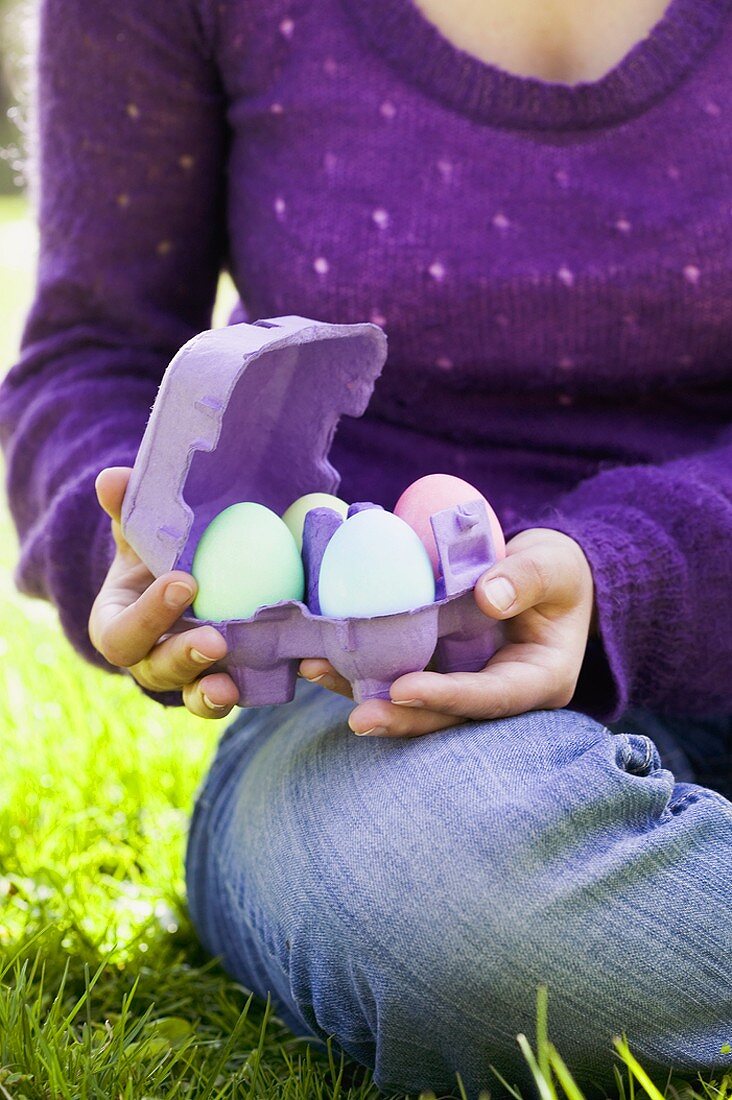 Frau sitzt mit gefärbten Eiern im Eierkarton auf Wiese