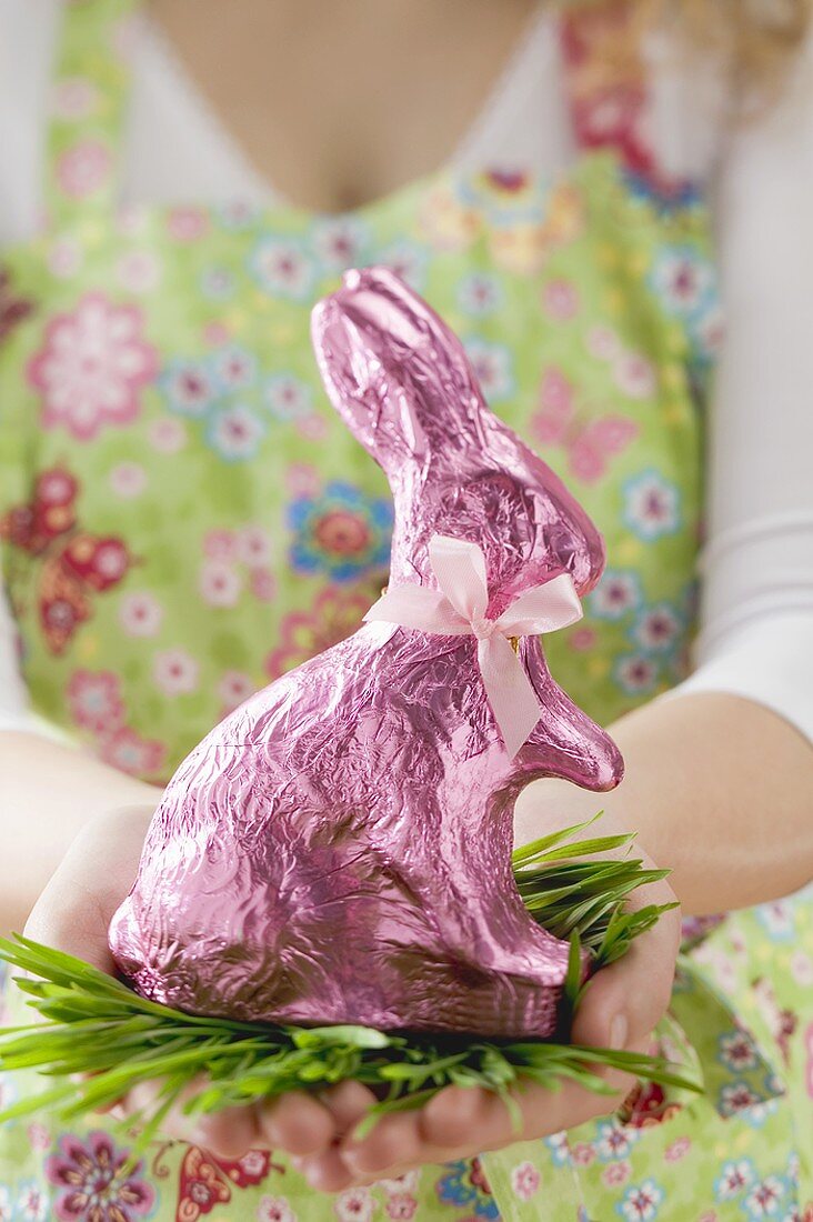 Frau hält in rosa Folie verpackten Osterhasen