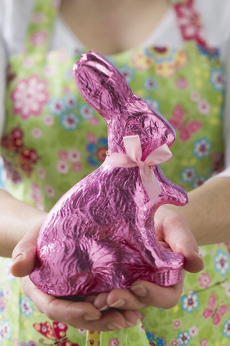 Frau hält in rosa Folie verpackten Osterhasen