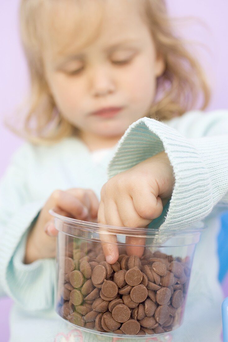 Small girl eating chocolate buttons out of plastic tub