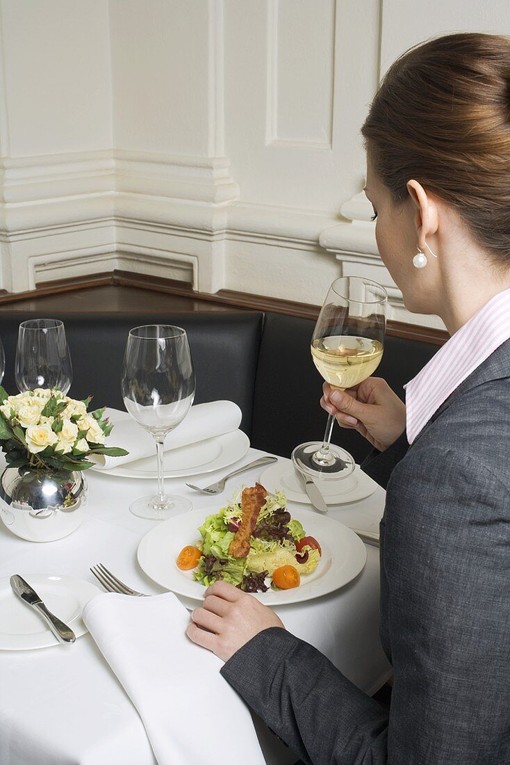 Frau trinkt Weißwein zum Salat im Restaurant