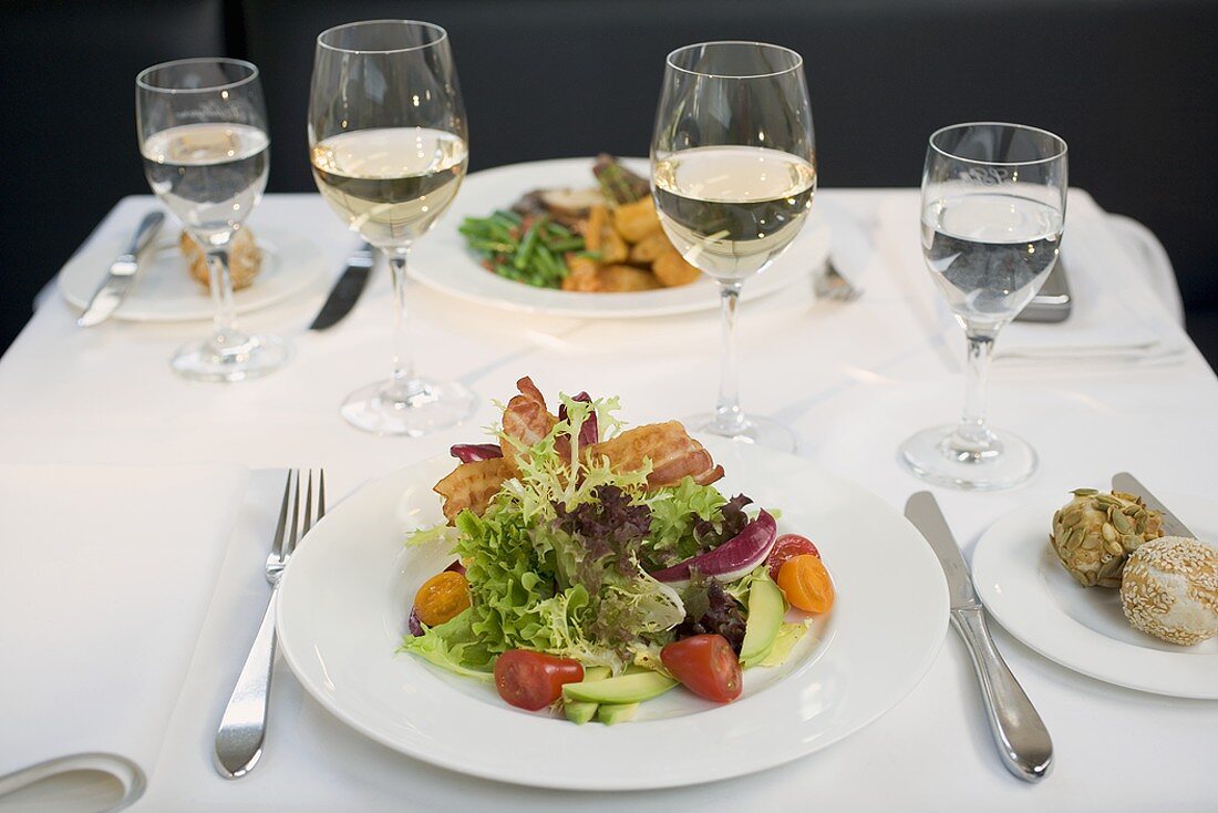 Blattsalat mit Bacon und Weissweingläser auf gedecktem Tisch
