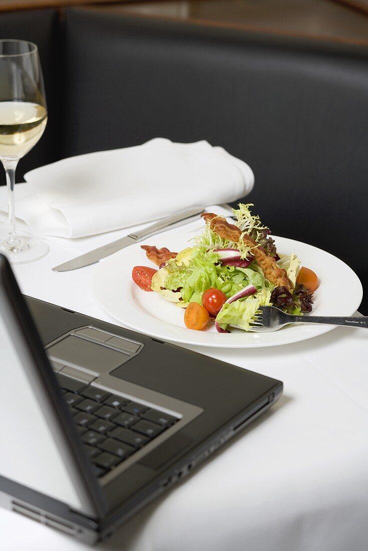 Blattsalat mit Bacon vor Laptop am Tisch im Restaurant