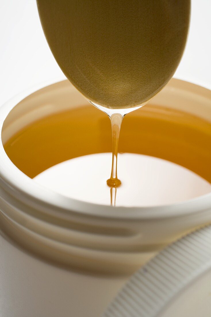 Honig tropft vom Kochlöffel in Plastikdose
