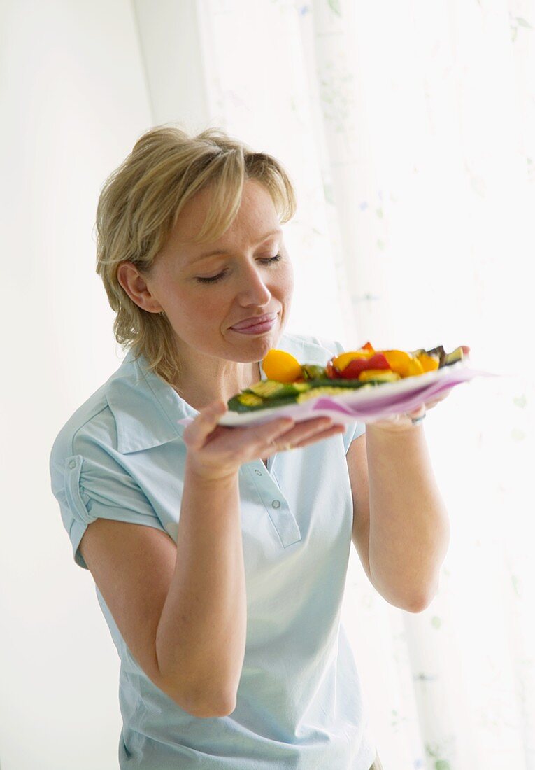 Frau riecht an gegrilltem Gemüse auf Teller