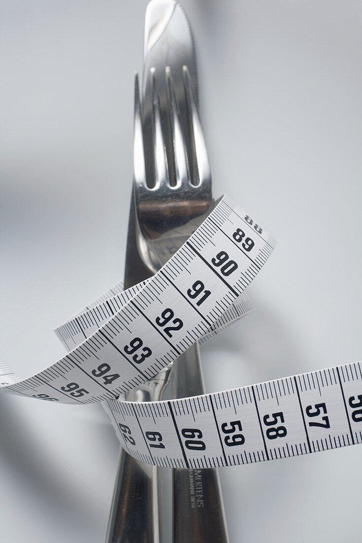 Knife and fork wrapped in tape measure on plate (close-up)