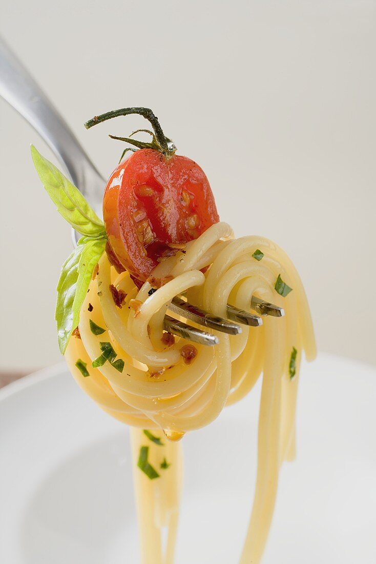 Spaghetti with cherry tomato on fork above white plate