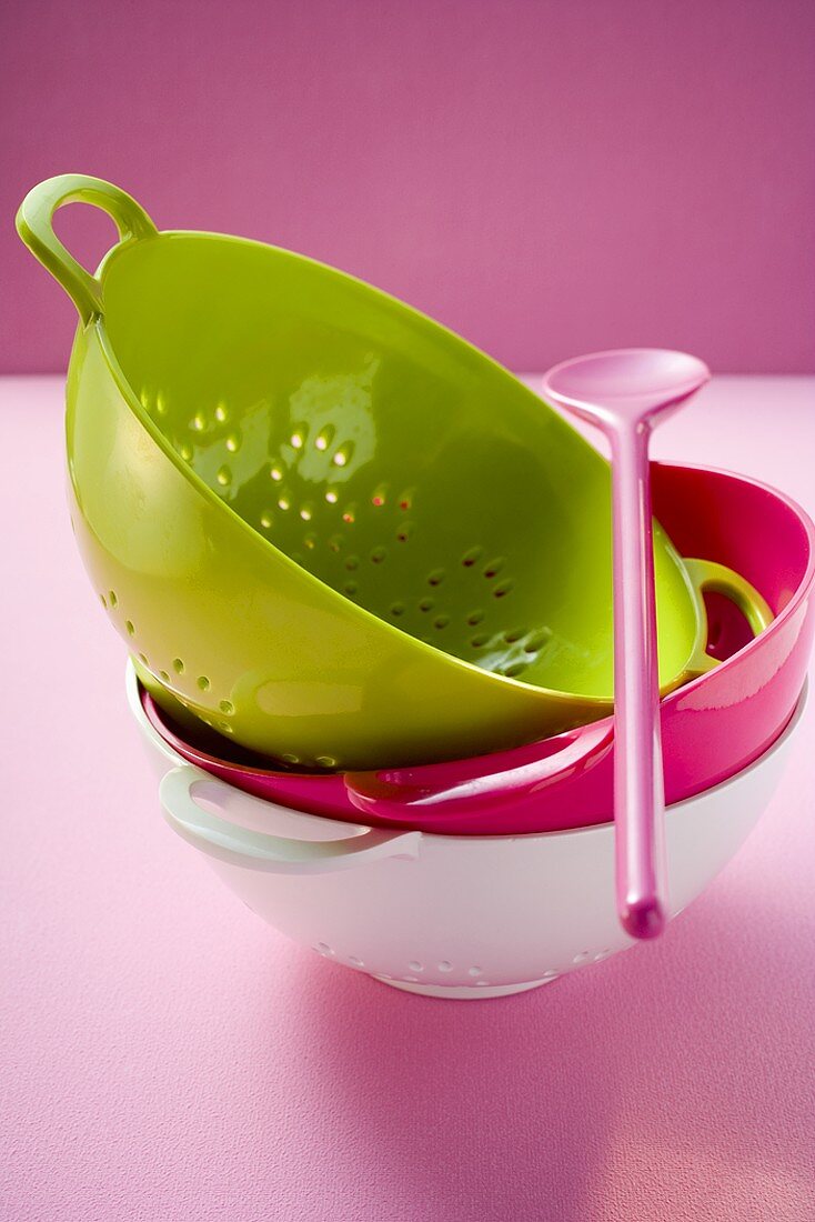 Coloured colanders, stacked, and pink cooking spoon