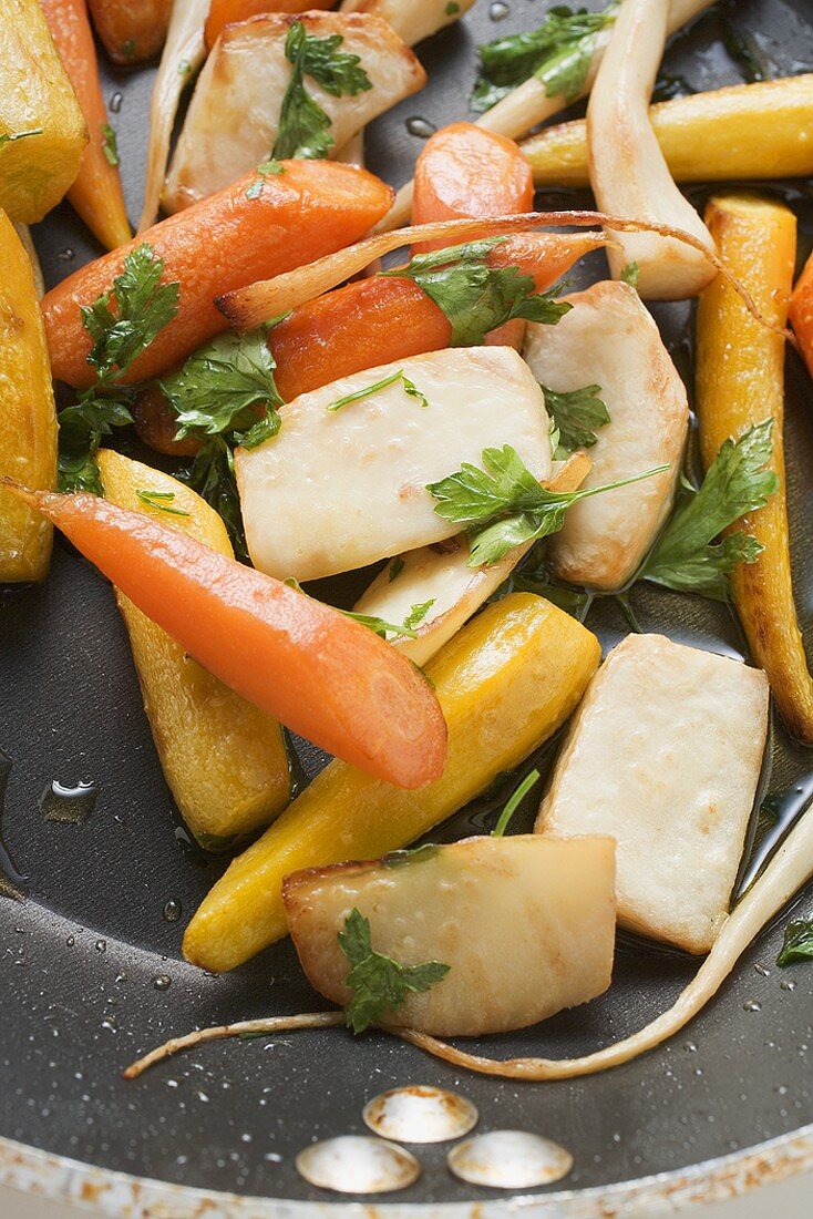 Fried root vegetables with parsley in frying pan