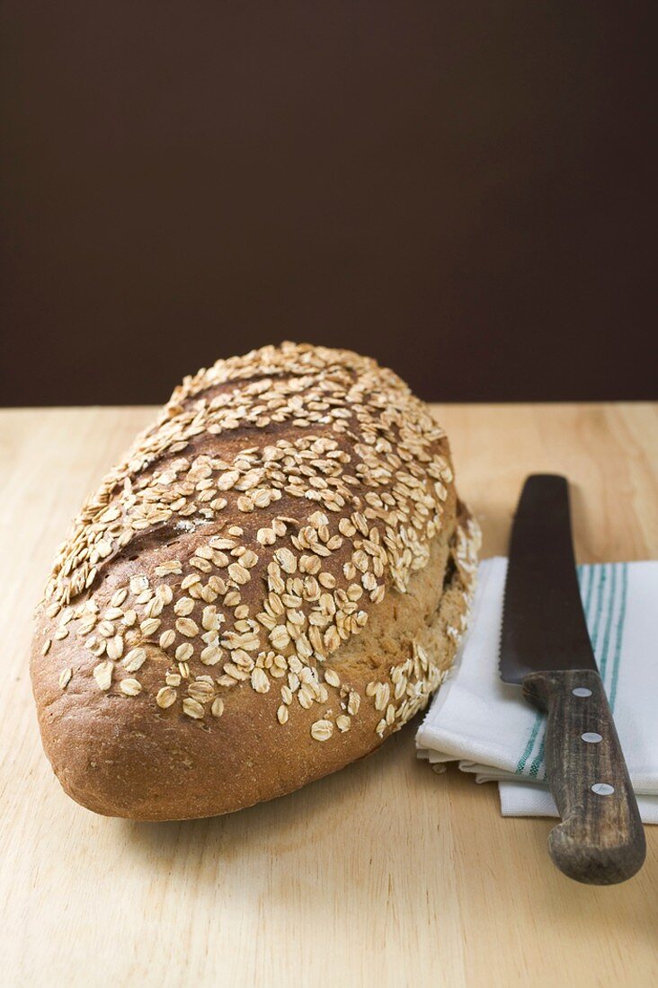 Wholemeal bread with rolled oats, tea towel, bread knife