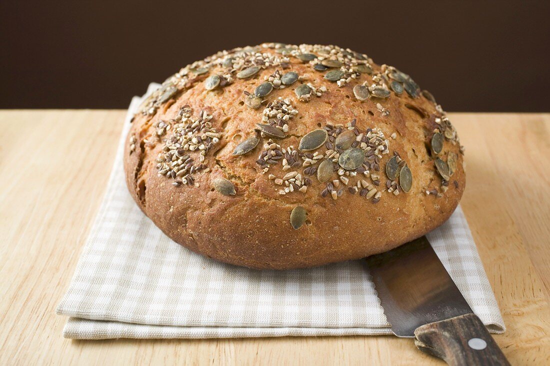 Vollkornbrot mit Kürbiskernen auf Geschirrtuch mit Brotmesser