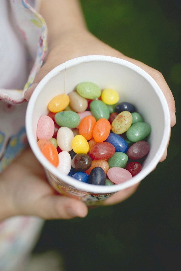 Kinderhände halten Becher mit bunten Zuckereiern