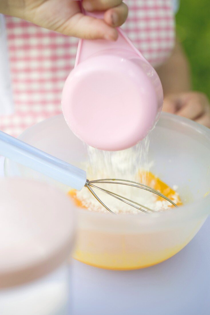 Child adding flour to egg yolks