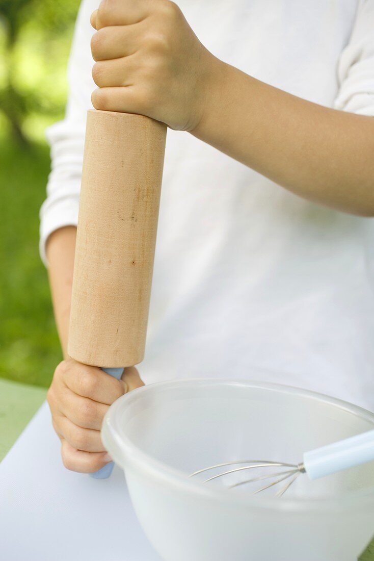 Child's hands holding rolling pin, bowl & whisk beside him
