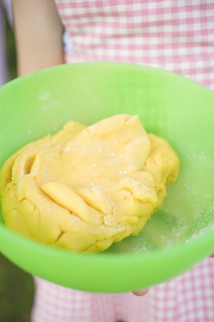 Child holding dough in green bowl