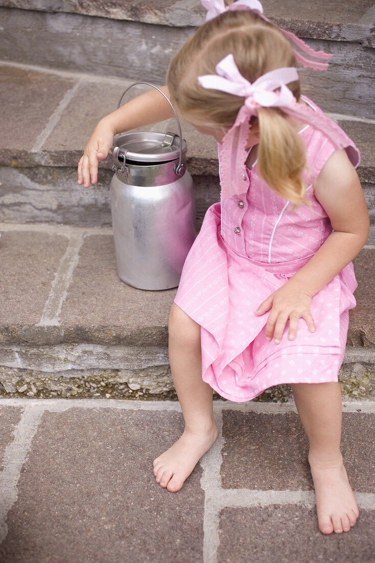 Kleines Mädchen auf Steinstufen mit Milchkanne
