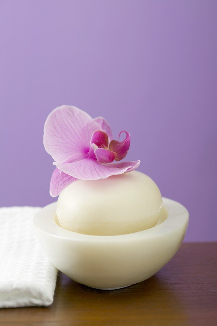 Orchid on soap in bowl beside white towel