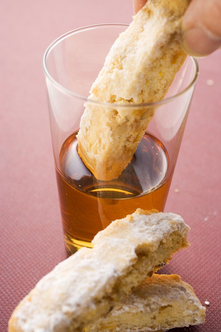 Hand dipping cantucci (Italian almond biscuit) into glass of Vin Santo