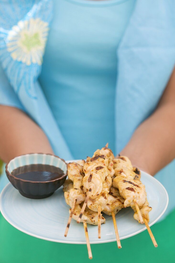 Woman holding plate of satay and soy sauce