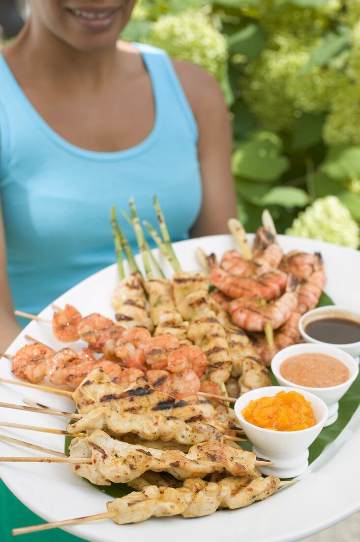 Frau hält grosse Platte mit Satespiessen und Dips