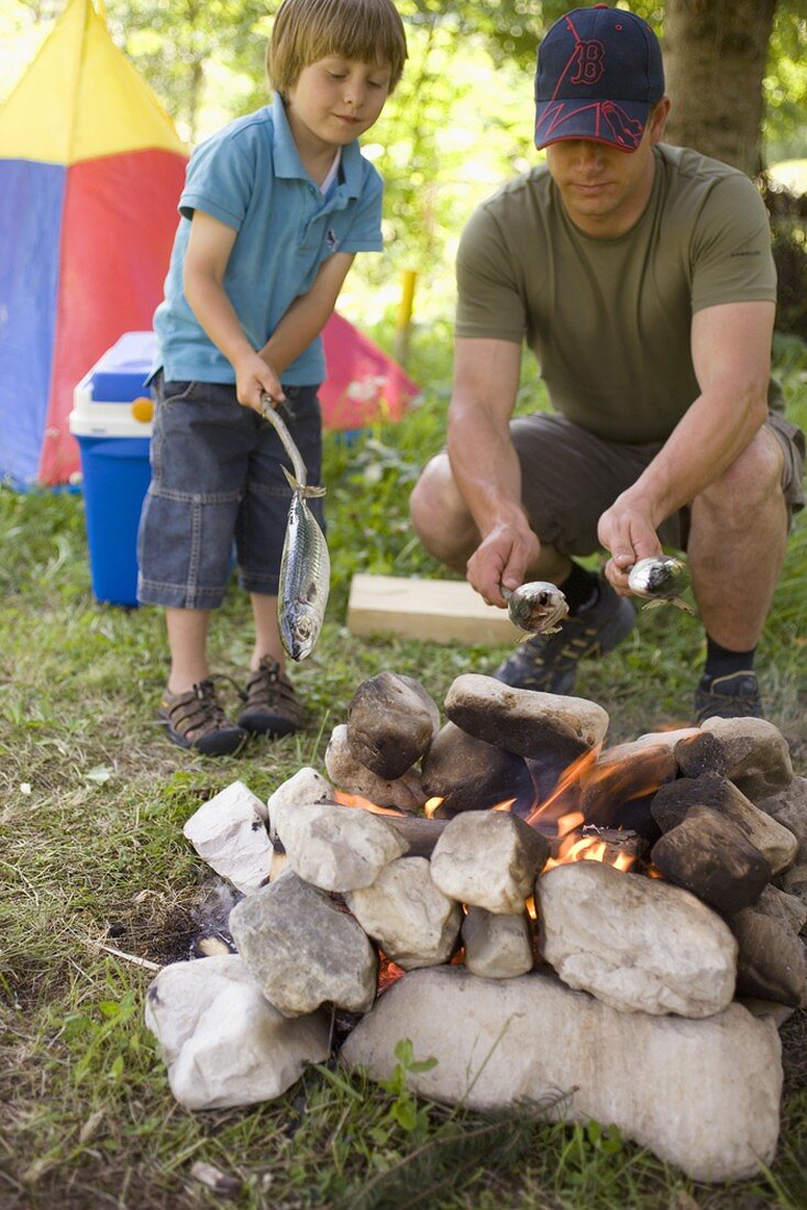 Father and son grilling fish over camp-fire