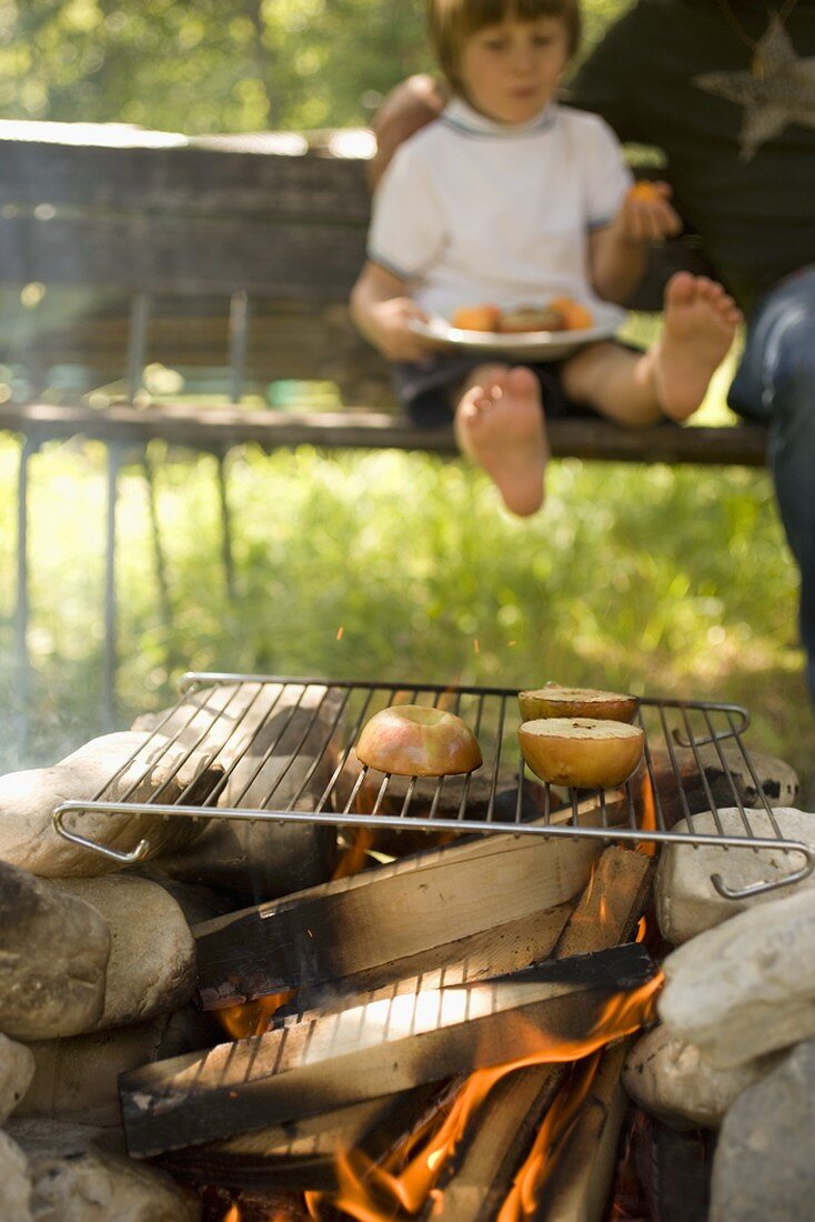 Apples on grill rack over camp-fire, child in background