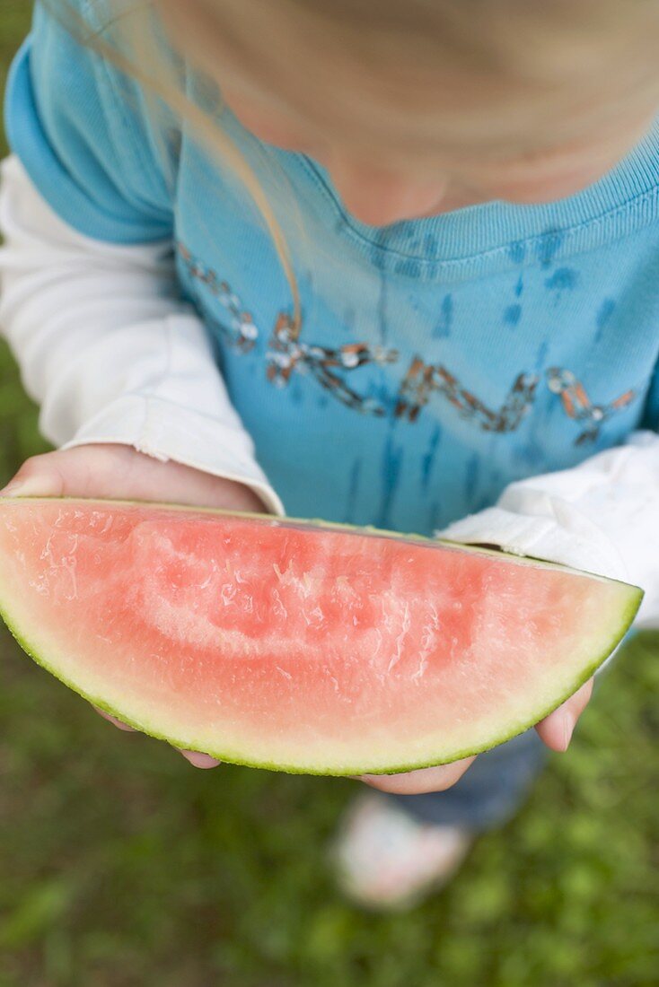 Small girl holding slice of watermelon with bites taken (overhead)