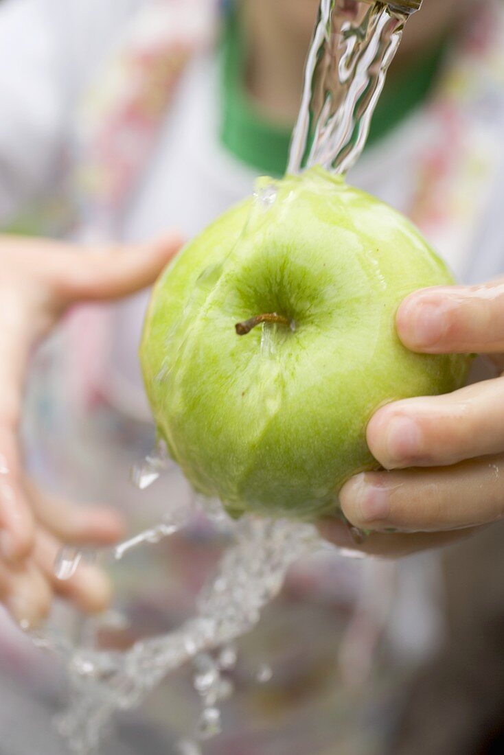 Kind hält grünen Apfel unter Wasserstrahl