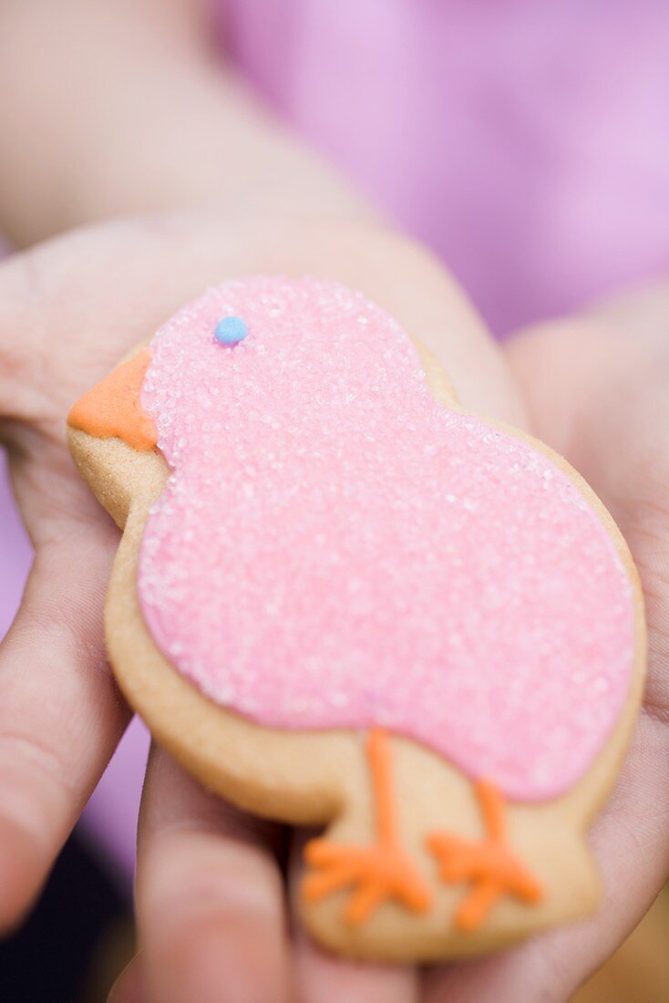 Kinderhand hält Osterplätzchen (rosa Küken)