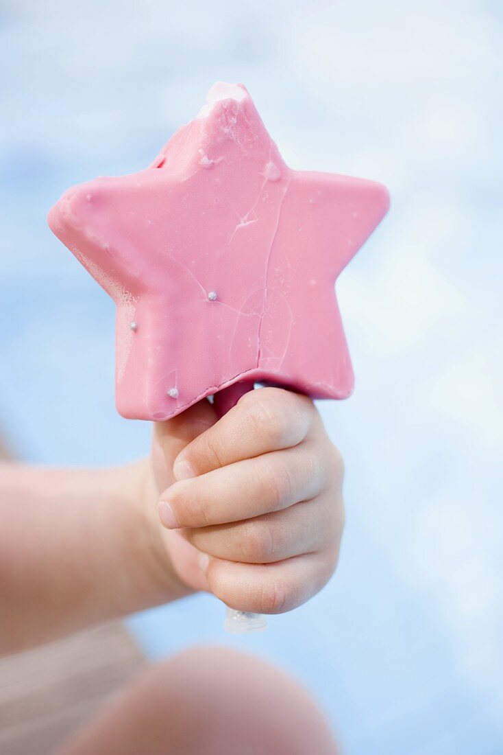 Kinderhand hält rosa Eis am Stiel