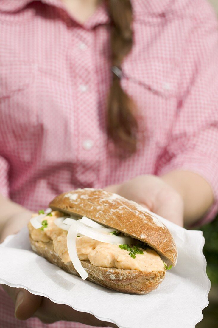 Woman holding bread roll with Obatzda (Camembert spread) & onions