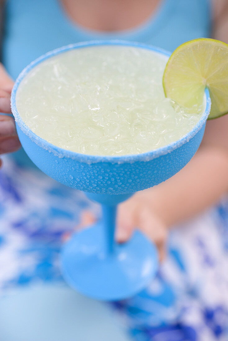 Frau hält türkisfarbenes Glas mit Limettencocktail