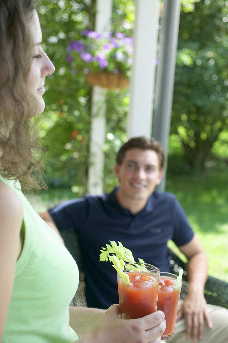 Young woman with two tomato drinks, man in background
