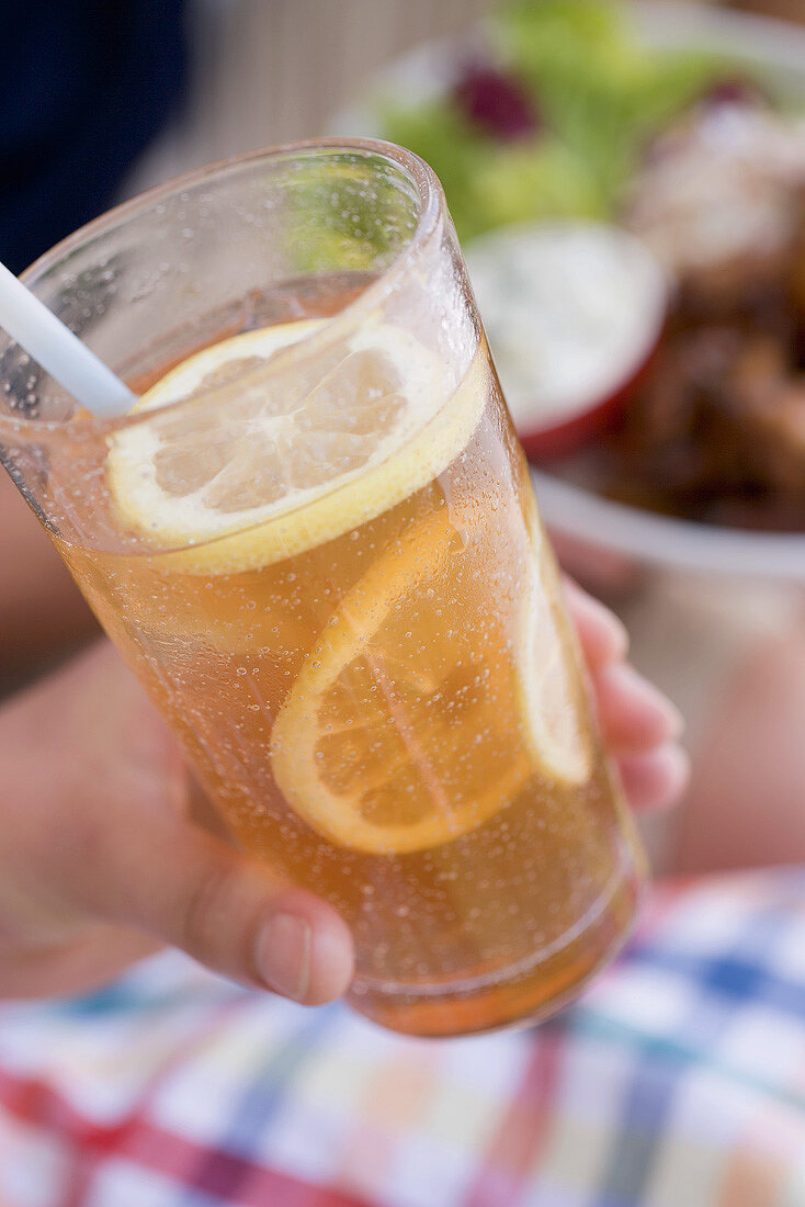 Hand holding a glass of iced tea with lemon slices