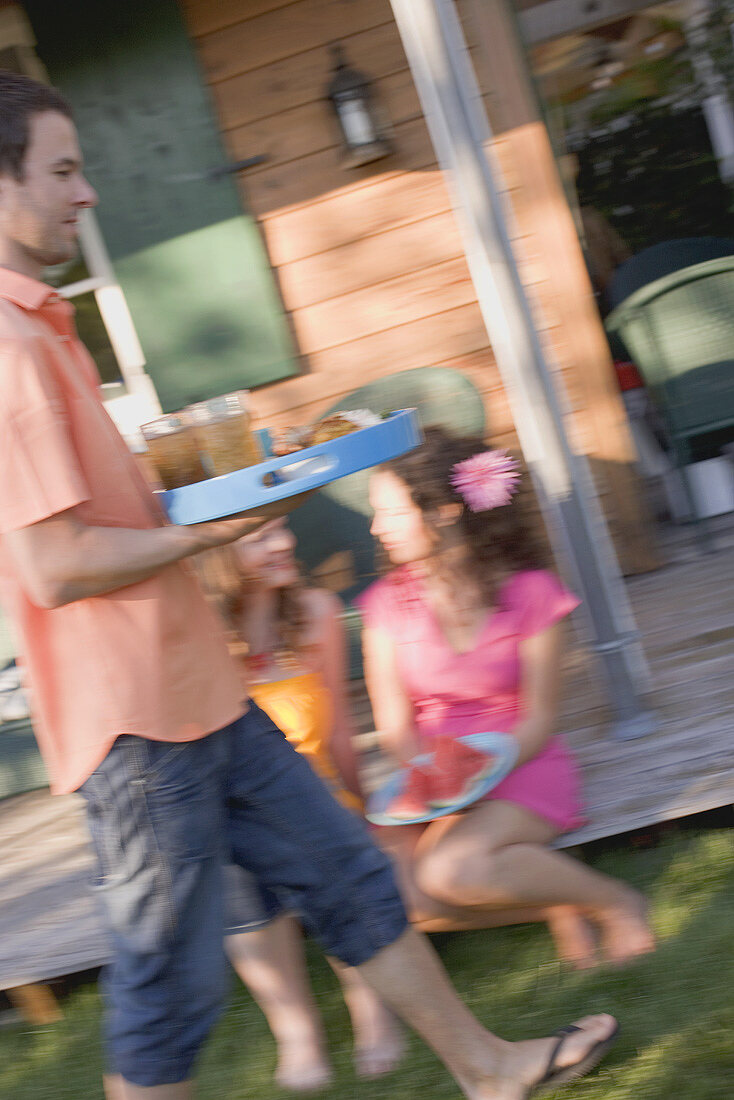 Mann serviert Tablett mit Eistee und Snacks im Garten