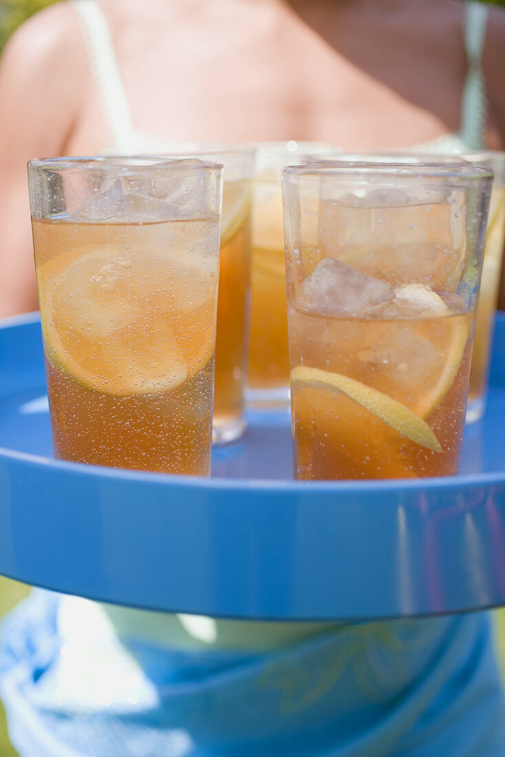 Several glasses of iced tea on tray, woman in background