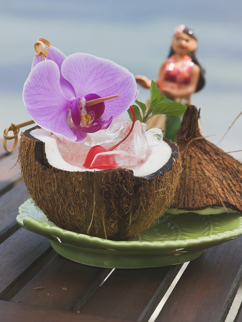 Kokosnusshälfte mit Eiswürfeln, Cocktailkirsche und Orchidee