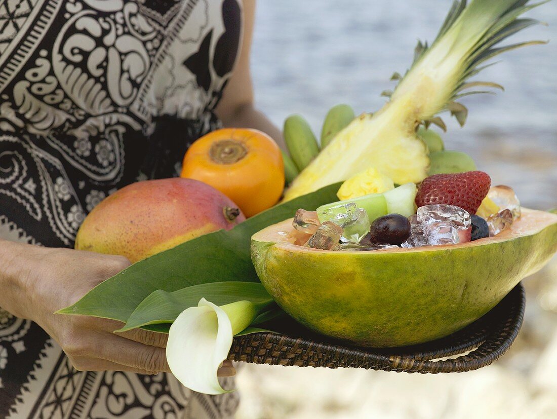 Woman holding tray of fresh exotic fruit by sea