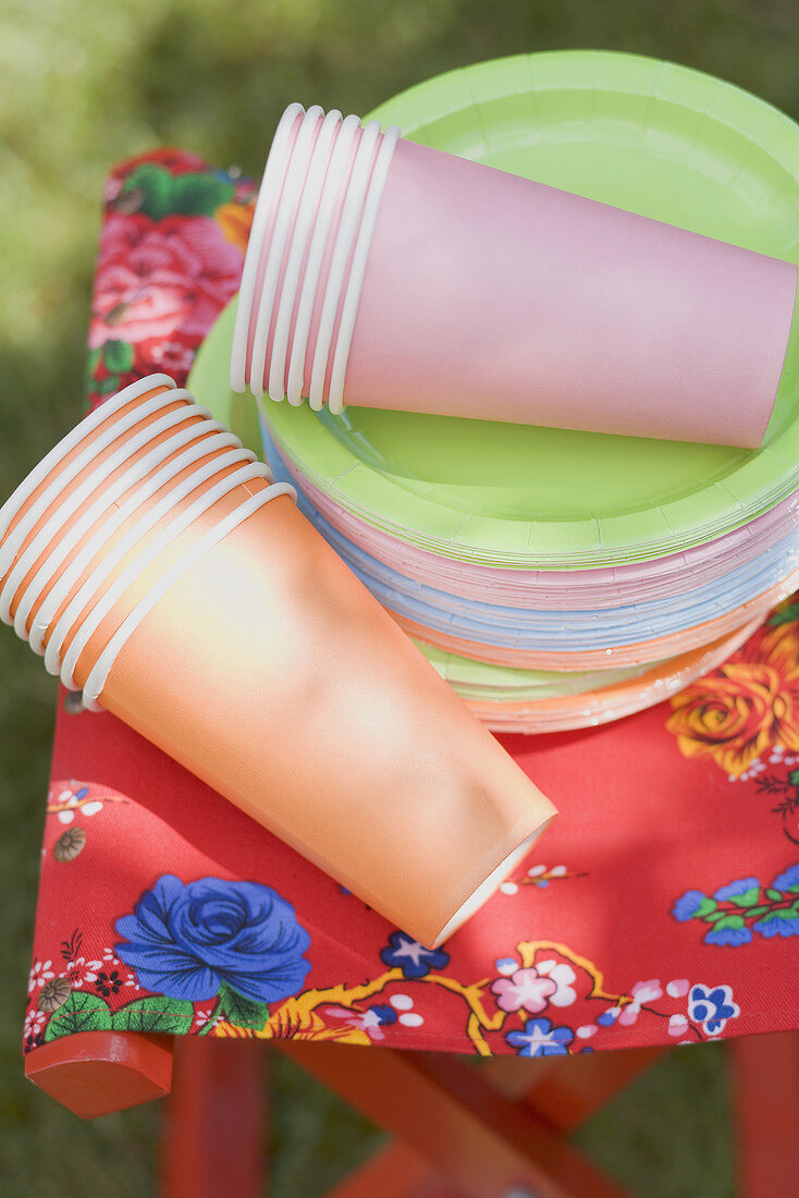 Coloured paper cups and plates on folding stool in garden