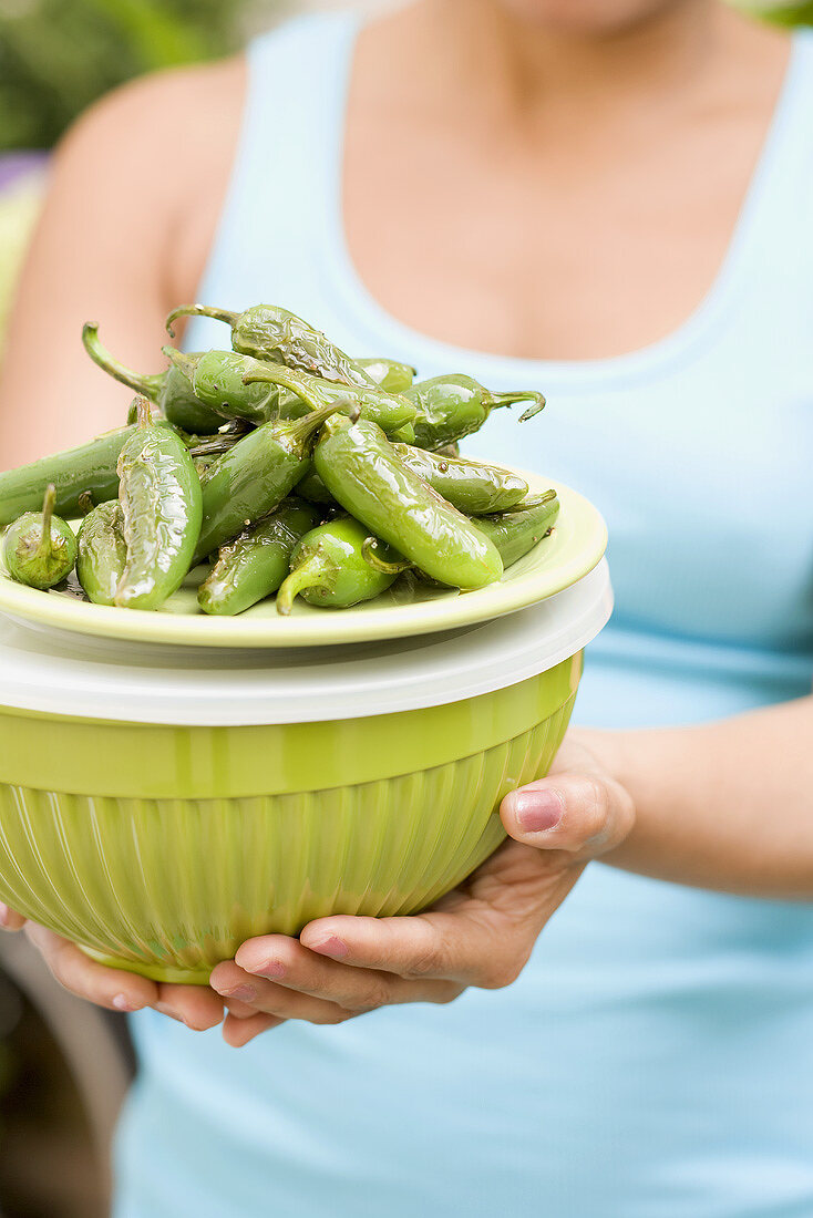 Woman holding grilled chillies on top of a green bowl