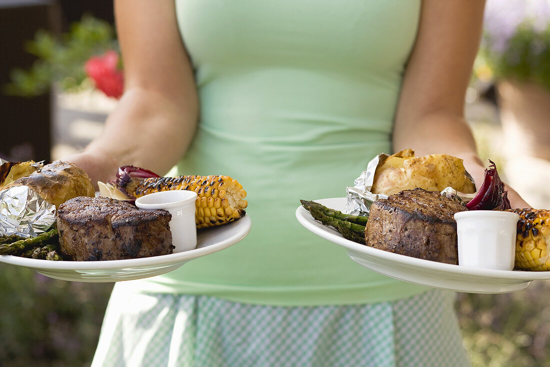 Woman serving two plates of grilled steak & accompaniments