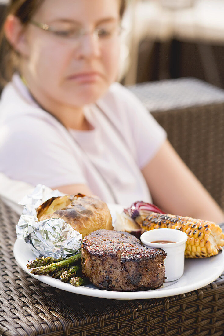 Grilled beef steak with accompaniments, woman in background