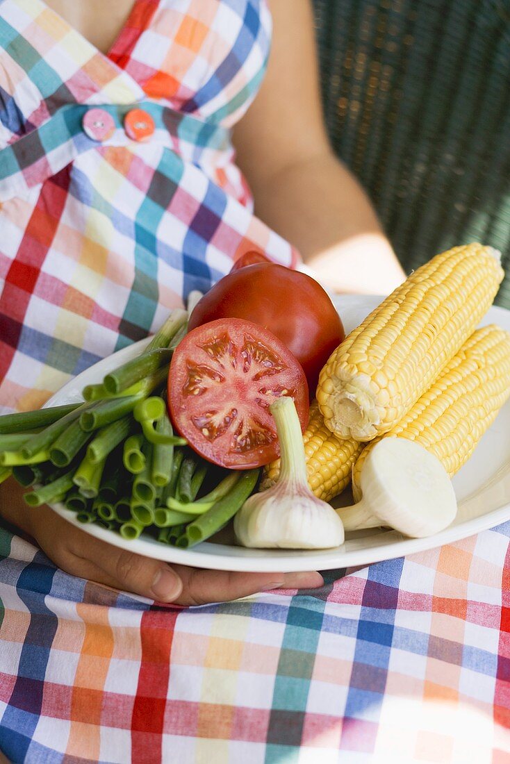 Woman holding plate of vegetables & corn on the cob for grilling